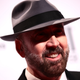 Nic Cage, in a black suit and gray fedora that shades his eyes, smiles at the crowd.